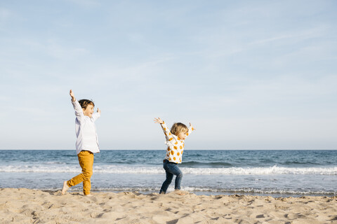 Glücklicher Junge und seine kleine Schwester laufen zusammen am Strand, lizenzfreies Stockfoto