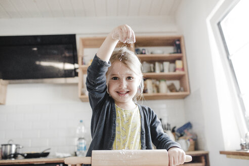 Porträt eines lächelnden kleinen Mädchens, das in der Küche Teig ausrollt - KMKF00901