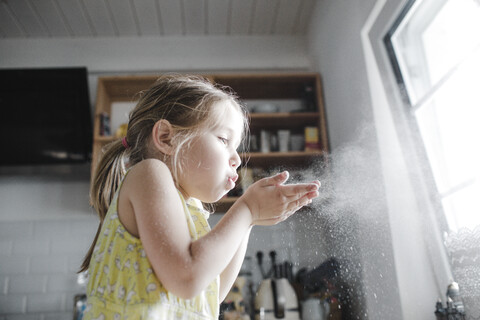 Kleines Mädchen bläst in der Küche Mehl in die Luft, lizenzfreies Stockfoto