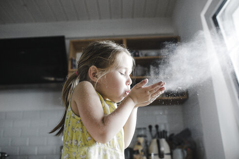 Little girl blowing flour in the air in the kitchen - KMKF00905
