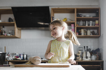Glückliches kleines Mädchen, das in der Küche Teig ausrollt - KMKF00906