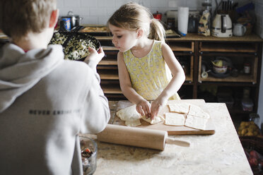 Kleines Mädchen und ihr älterer Bruder bereiten in der Küche gefülltes Gebäck zu - KMKF00911