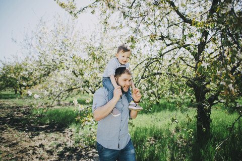 Kaukasischer Vater und Sohn gehen in der Nähe eines Baumes, lizenzfreies Stockfoto