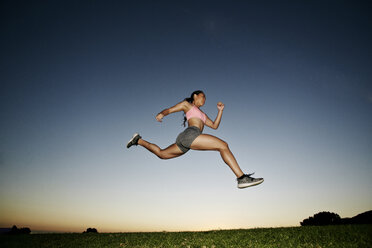 Gemischtrassige Frau läuft und springt im Feld bei Sonnenuntergang - BLEF02112