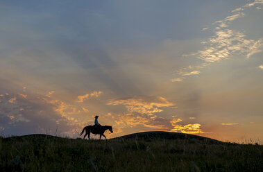 Silhouette einer kaukasischen Frau auf einem Pferd bei Sonnenuntergang - BLEF02148