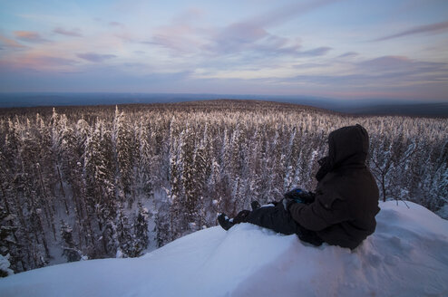 Kaukasischer Mann sitzt im Schnee und bewundert die malerische Aussicht auf den Wald - BLEF02216