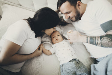 Caucasian mother and father holding hands with baby son on bed - BLEF02242