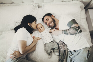 Caucasian mother and father holding hands with baby son on bed - BLEF02243