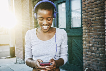 Smiling Black woman listening to cell phone with headphones in city - BLEF02250