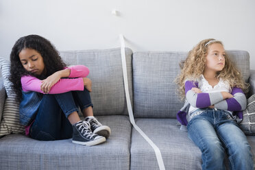 Frustrated girls dividing sofa with tape - BLEF02298