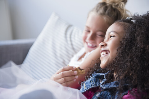 Lächelnde Mädchen essen Kekse auf dem Sofa, lizenzfreies Stockfoto