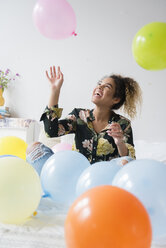 Mixed Race woman sitting on bed playing with balloons - BLEF02328