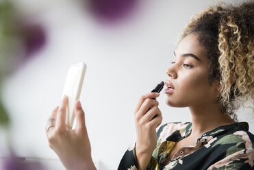 Mixed-Race-Frau hält Handy und trägt Lippenstift auf - BLEF02332