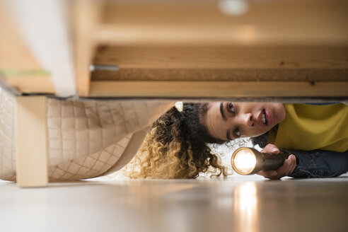 Gemischtrassige Frau sucht unter dem Bett mit Taschenlampe - BLEF02343