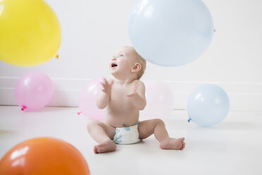 Kaukasischer kleiner Junge sitzt auf dem Boden und beobachtet Ballons - BLEF02352