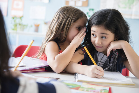 Mädchen flüstert einem Klassenkameraden in der Schule zu - BLEF02358