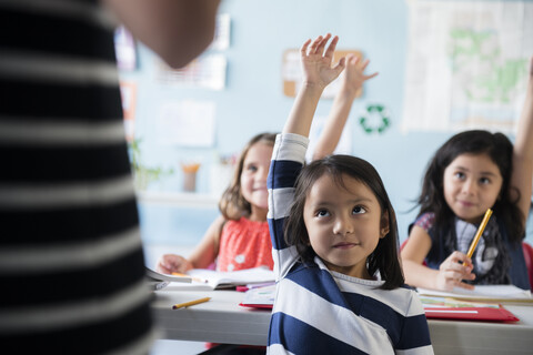 Girls raising hand for teacher in classroom stock photo