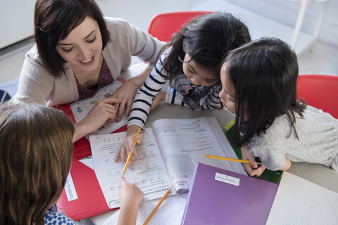 Lehrerin hilft Mädchen mit dem Arbeitsbuch im Klassenzimmer, lizenzfreies Stockfoto
