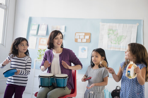 Lehrerin und Mädchen spielen Bongos und Tamburine im Klassenzimmer - BLEF02371