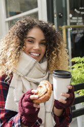 Lächelnde Mixed Race Frau zeigt Donut und Kaffeetasse - BLEF02401