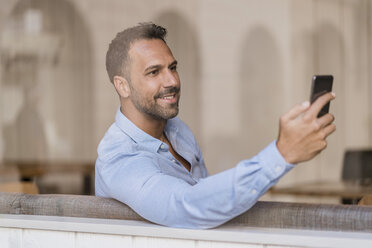 Lächelnder Geschäftsmann mit Mobiltelefon hinter einer Fensterscheibe - DIGF06935