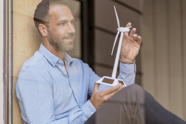 Businessman with wind turbine model behind windowpane - DIGF06936