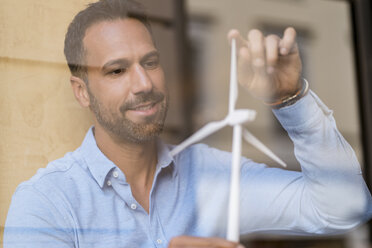 Businessman with wind turbine model behind windowpane - DIGF06937