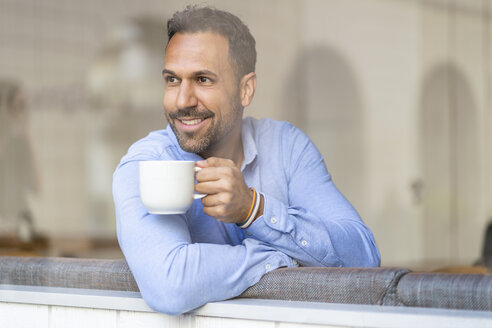 Lächelnder Geschäftsmann mit einer Tasse Kaffee und Blick aus dem Fenster - DIGF06943