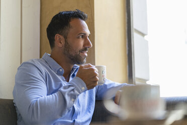 Lächelnder Geschäftsmann mit einer Tasse Kaffee und Blick aus dem Fenster - DIGF06952