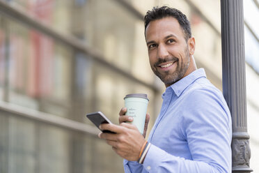 Lächelnder Geschäftsmann mit Kaffee zum Mitnehmen und Mobiltelefon in der Stadt - DIGF06956
