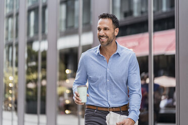 Businessman with takeaway coffee and newspaper in the city on the go - DIGF06973