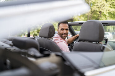 Man sitting in car with closing convertible top - DIGF06988