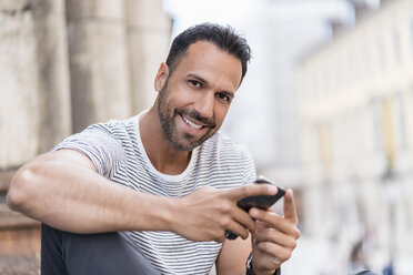 Portrait of smiling man with cell phone in the city - DIGF06991