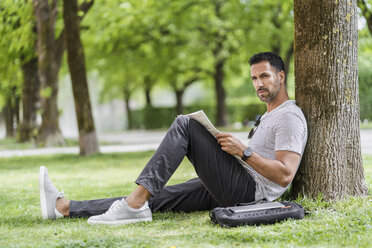 Man leaning against a tree in park reading newspaper - DIGF07001