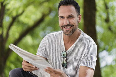 Porträt eines lächelnden Mannes, der im Park Zeitung liest - DIGF07013