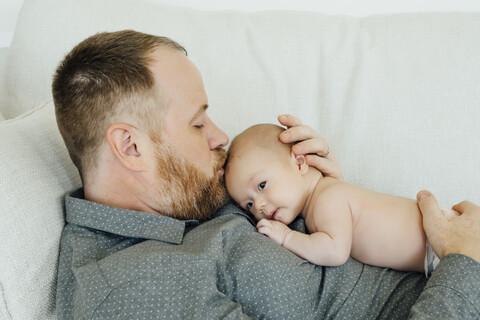 Vater liegt auf dem Sofa und küsst seine kleine Tochter auf den Kopf, lizenzfreies Stockfoto