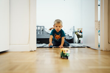 Boy kneeling on floor pushing toy cars - BLEF02492