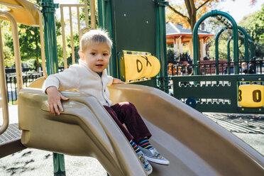 Porträt eines gemischtrassigen Jungen, der auf einer Spielplatzrutsche sitzt - BLEF02498