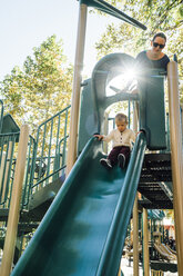 Mother watching son on playground slide - BLEF02499