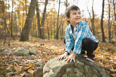 Lächelnder Mixed-Race-Junge, der im Herbst auf einem Felsen hockt - BLEF02719