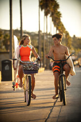 Teenager und Mädchen auf Fahrrädern mit Surfbrettern - BLEF02744