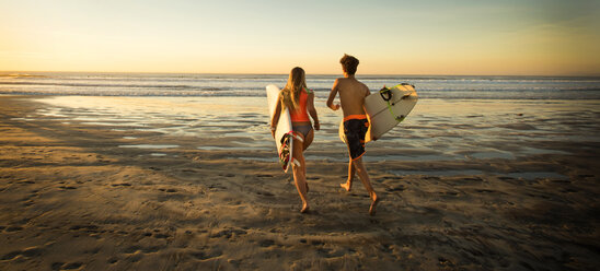 Teenage boy and girl carrying surfboards running to ocean - BLEF02748