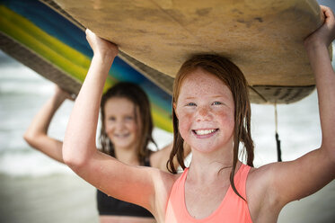 Portrait of smiling girls balancing surfboards on top of heads - BLEF02761
