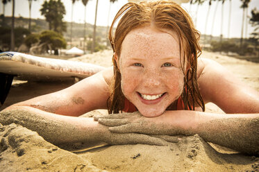 Porträt eines lächelnden Mädchens, das am Strand liegt und mit Sand bedeckt ist - BLEF02763