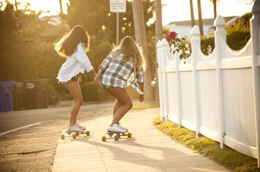 Teenage girls skateboarding on sidewalk - BLEF02769