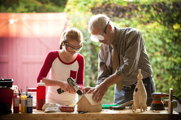 Grandfather helping granddaughter build birdhouse in garage - BLEF02776