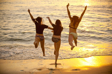 Teenage girls running into ocean at sunset - BLEF02807