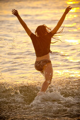 Teenage girl running into ocean at sunset - BLEF02808