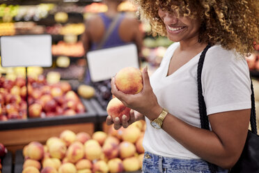 Black woman examining peaches in grocery store - BLEF02816