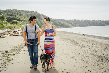 Pregnant lesbian couple walking dog on beach - BLEF02852